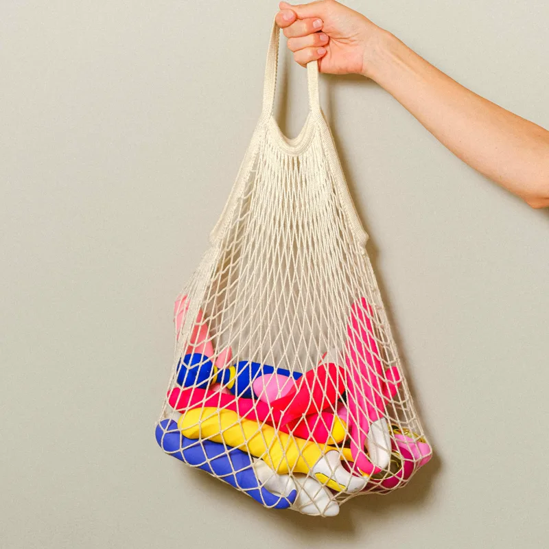 Una mano sostiene una bolsa de red llena de piezas de colores